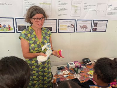 A woman stands at the front of a classroom holding period products.